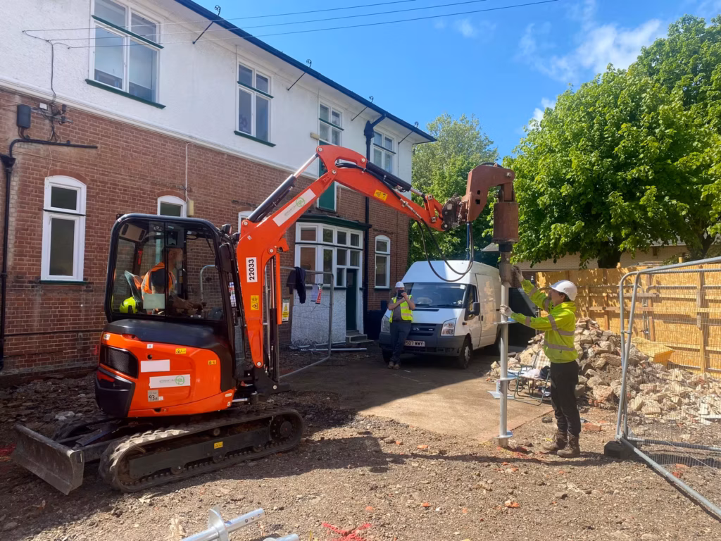 Mini excavator installing a screw pile beside a residential property